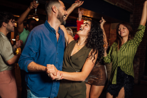 A close up of a couple who are dancing with each other as they enjoy a night out with their friends. They are being cheered on by their friends as they have a fun time together.